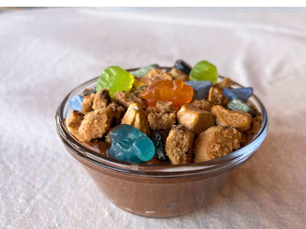 a small bowl filled with layers of pudding, crushed cookies and gummy dinosaurs