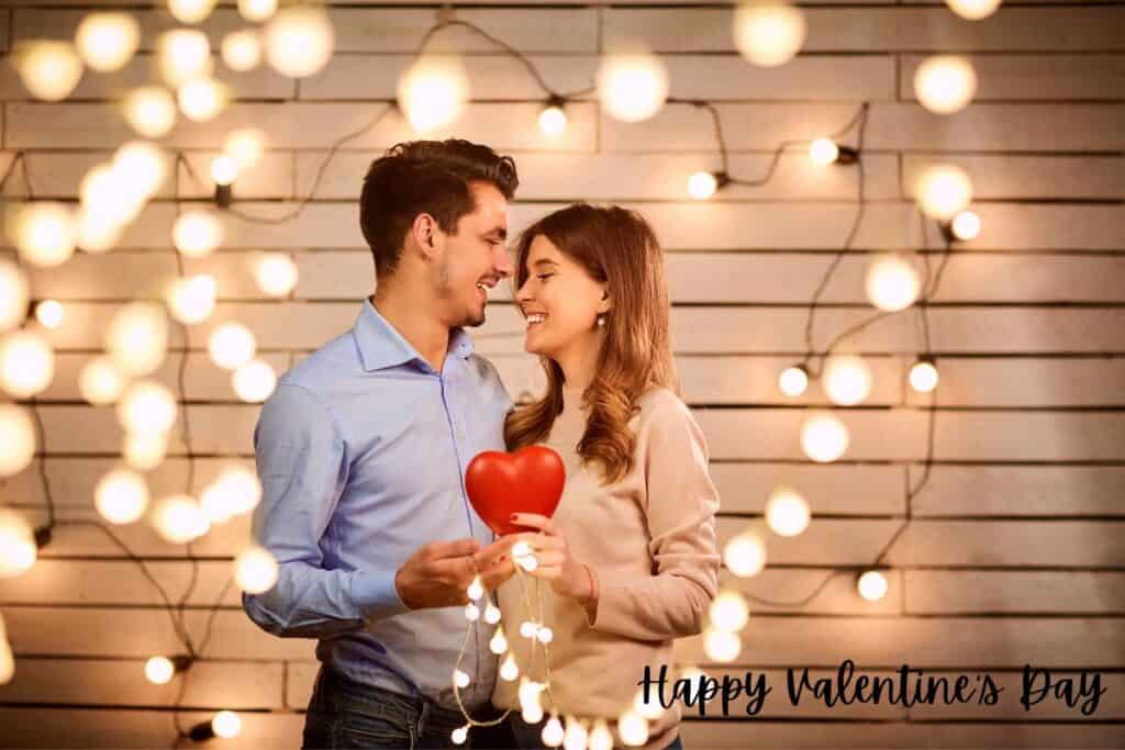 Man and woman smiling at each other holding a red heart between them celebrating Valentine's Day