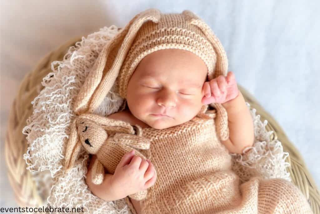 A baby sleeping, holding a stuffed bunny from his Easter basket and wearing a cute outfit along with bunny ears hat demonstrating a great easter portrait idea. 